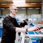 Zu sehen ist ein Mitarbeiter in einer Produktionshalle, der ein Fenster prüft und bearbeitet