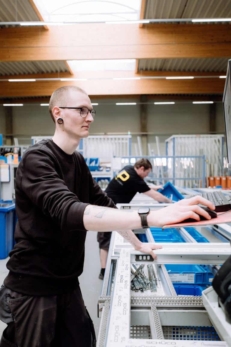 Zu sehen ist ein Mitarbeiter in einer Produktionshalle, der ein Fenster prüft und bearbeitet