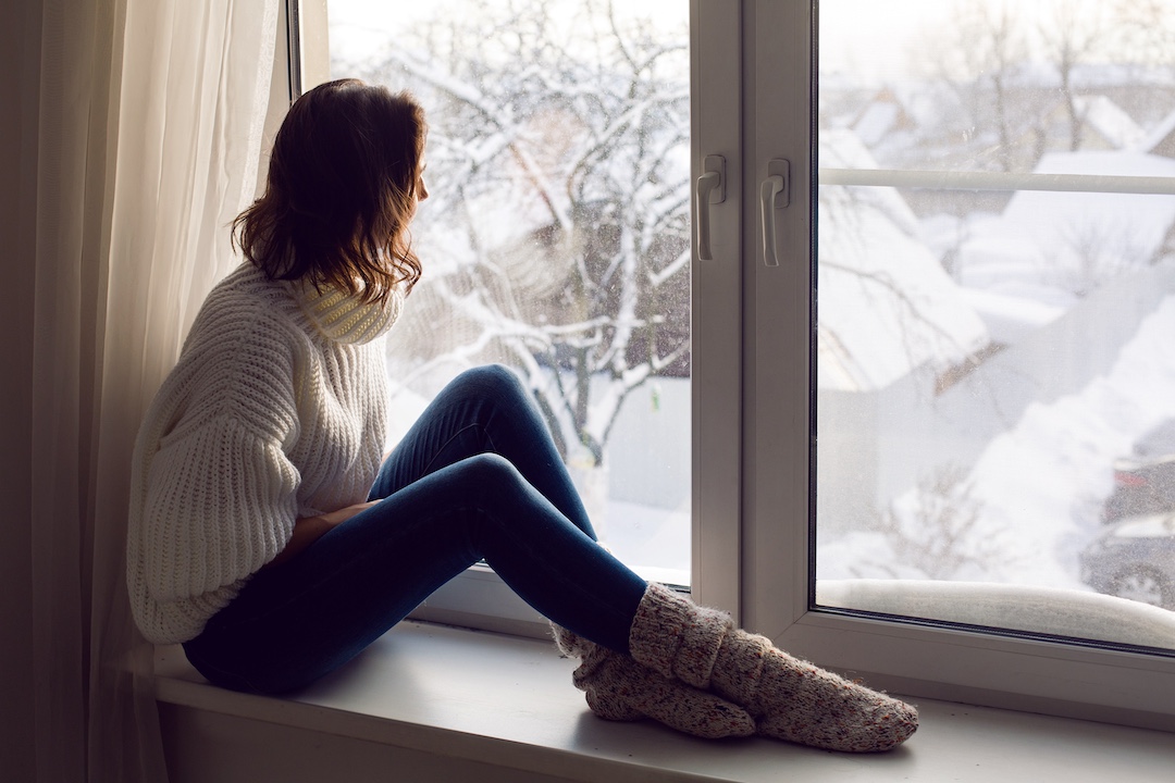 Frau sitzend am Fenster vor Winterlandschaft